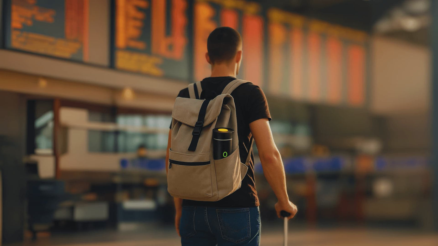 Traveler at airport with NØMA portable espresso maker in backpack, perfect for flights and layovers.